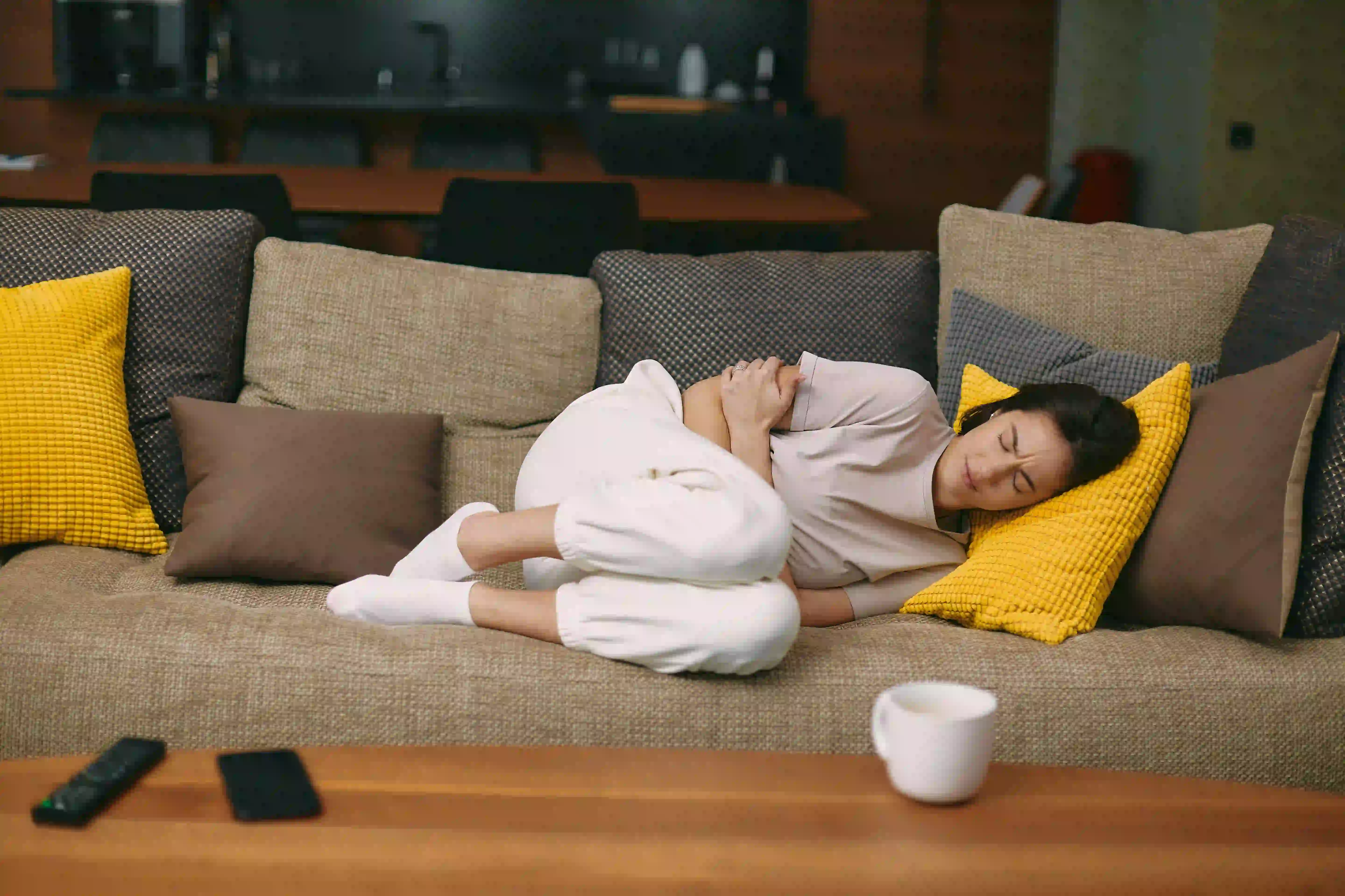 Women holding chest on couch with coffee cup on counter Women holding chest on couch with coffee cup on counter